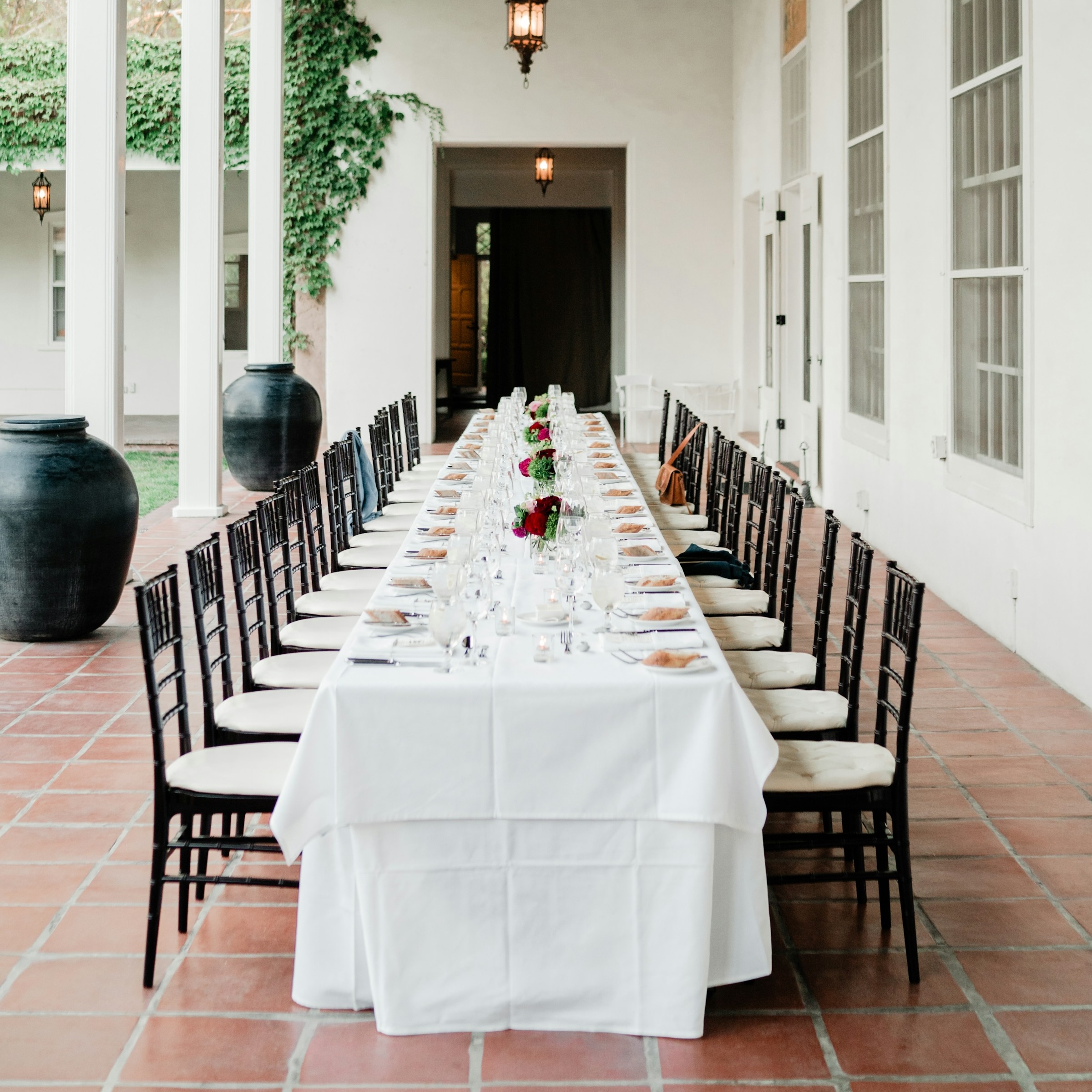 Wedding reception dinner with long table and chairs, setup with tableware and flowers on patio of large manor