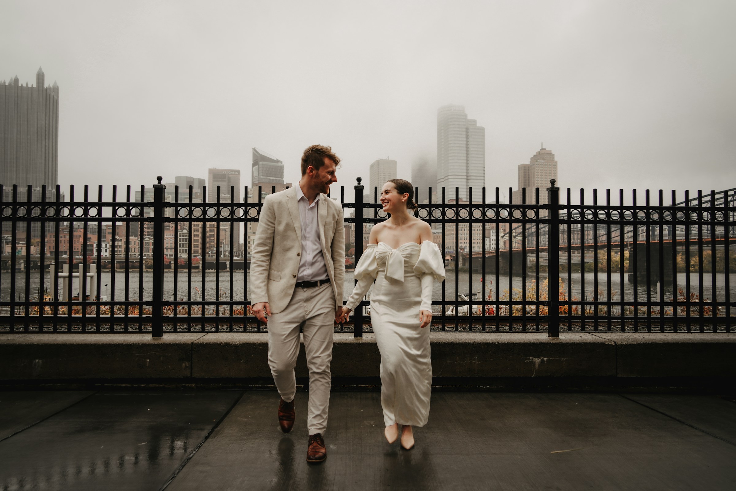 Couple walking towards camera with city skyline covered in fog on horizon