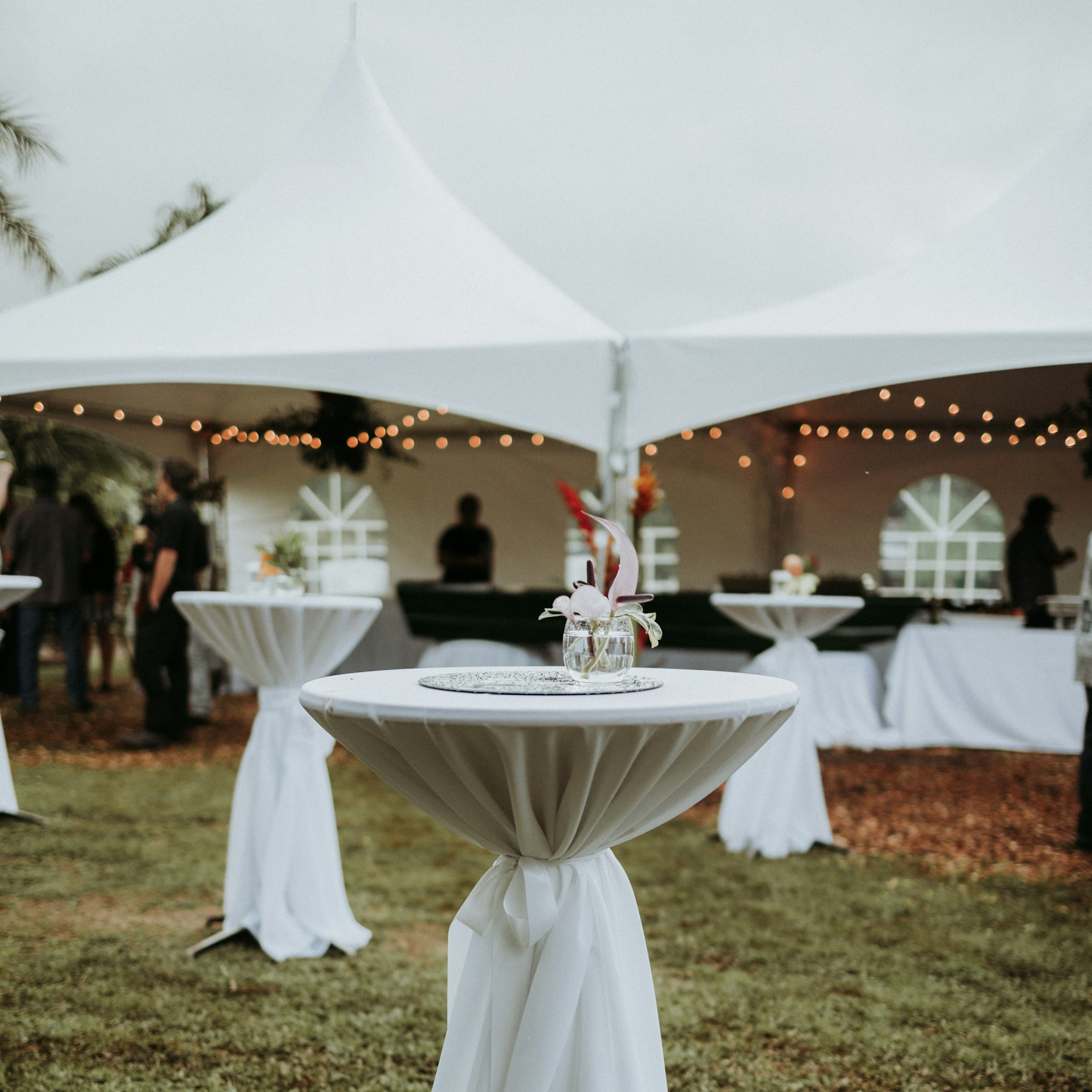 White rental wedding tent set up with white linen tables in front and string lights