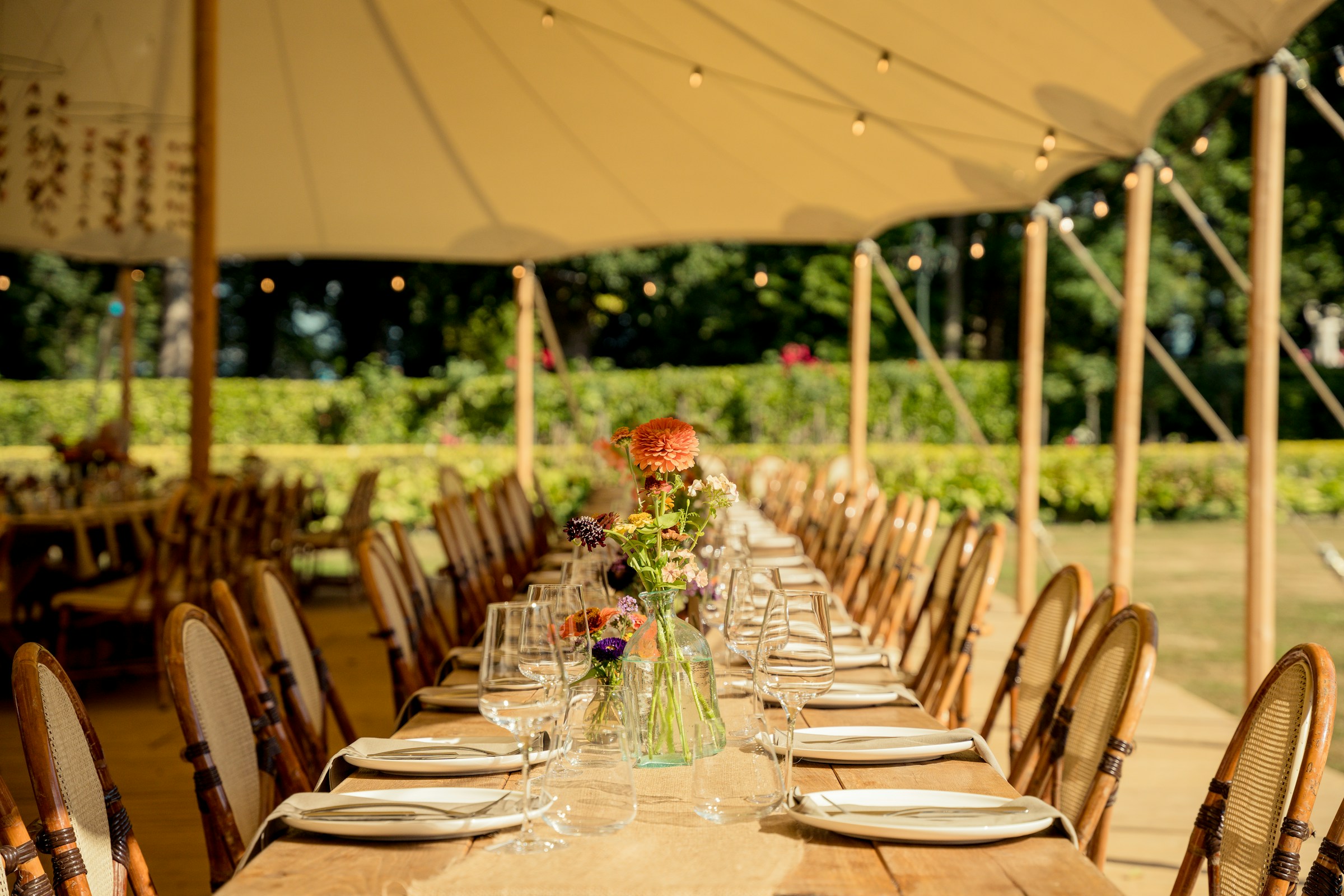 Wedding reception dinner under white tent, set up with chairs, tables, linens, and tableware