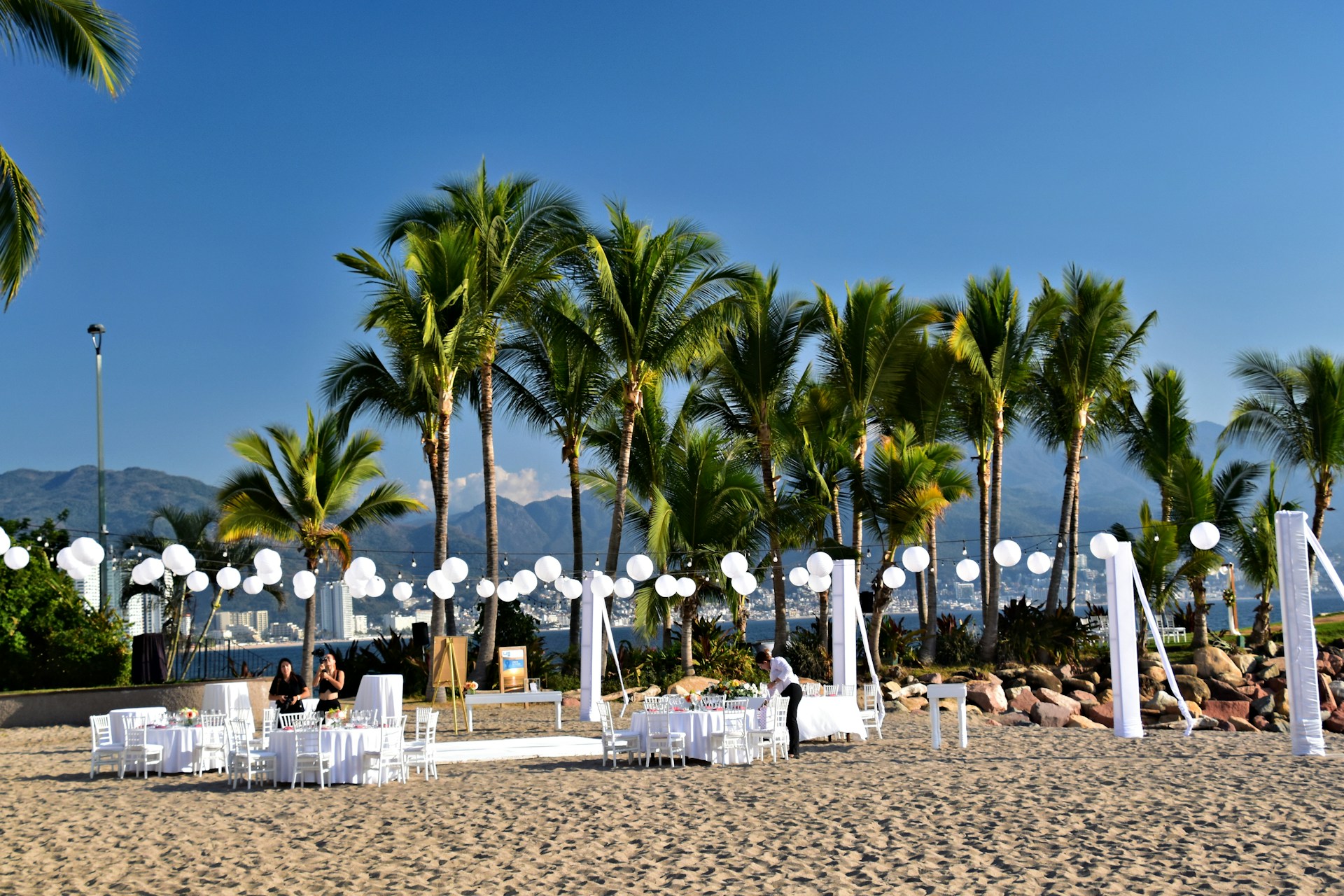 Beach wedding venue with white tables, chairs, string lights, and carepet in Europe